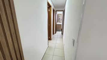 A narrow hallway with white walls and wooden doors, leading to a bathroom with a toilet and sink.