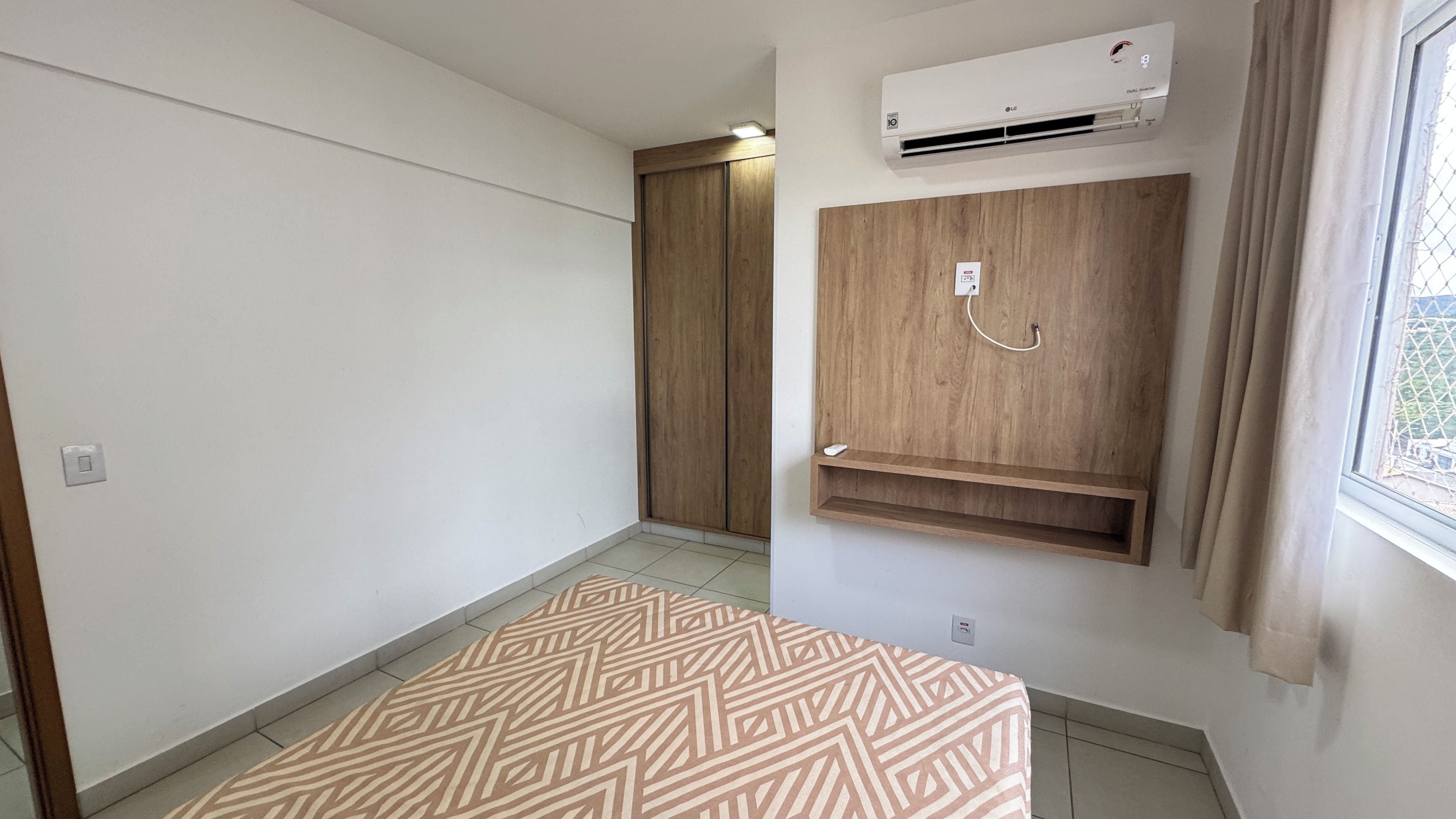 Una habitación con alfombra estampada, un equipo de aire acondicionado, un armario de madera y una ventana con cortinas.
