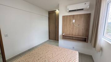 A room with a patterned rug, an air conditioning unit, a wooden wardrobe, and a window with curtains.