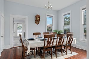 A dining room with a table set for six, wooden chairs, a chandelier, and a clock on the wall. - NEW! Fall in a Victorian | Grand Porches Near DT (San Antonio)