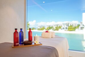 Una camera d'albergo con un'ampia finestra che si affaccia su una spiaggia, un vassoio con articoli da toilette e una candela.