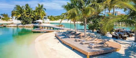 A beach resort with a wooden deck, lounge chairs, and palm trees.