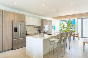 Une cuisine moderne dotée d’un grand îlot central, d’appareils électroménagers en acier inoxydable et d’un coin repas avec des chaises en osier.