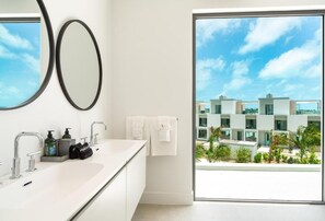 Un baño moderno con dos lavamanos, un espejo grande y vistas a una zona residencial a través de una puerta de cristal.