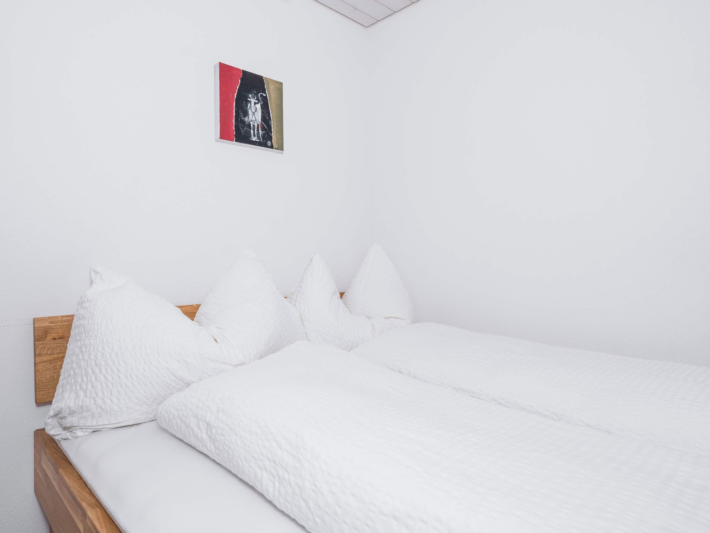 Un lit simple avec une literie et des oreillers blancs, une tête de lit en bois et une œuvre d’art accrochée au mur.