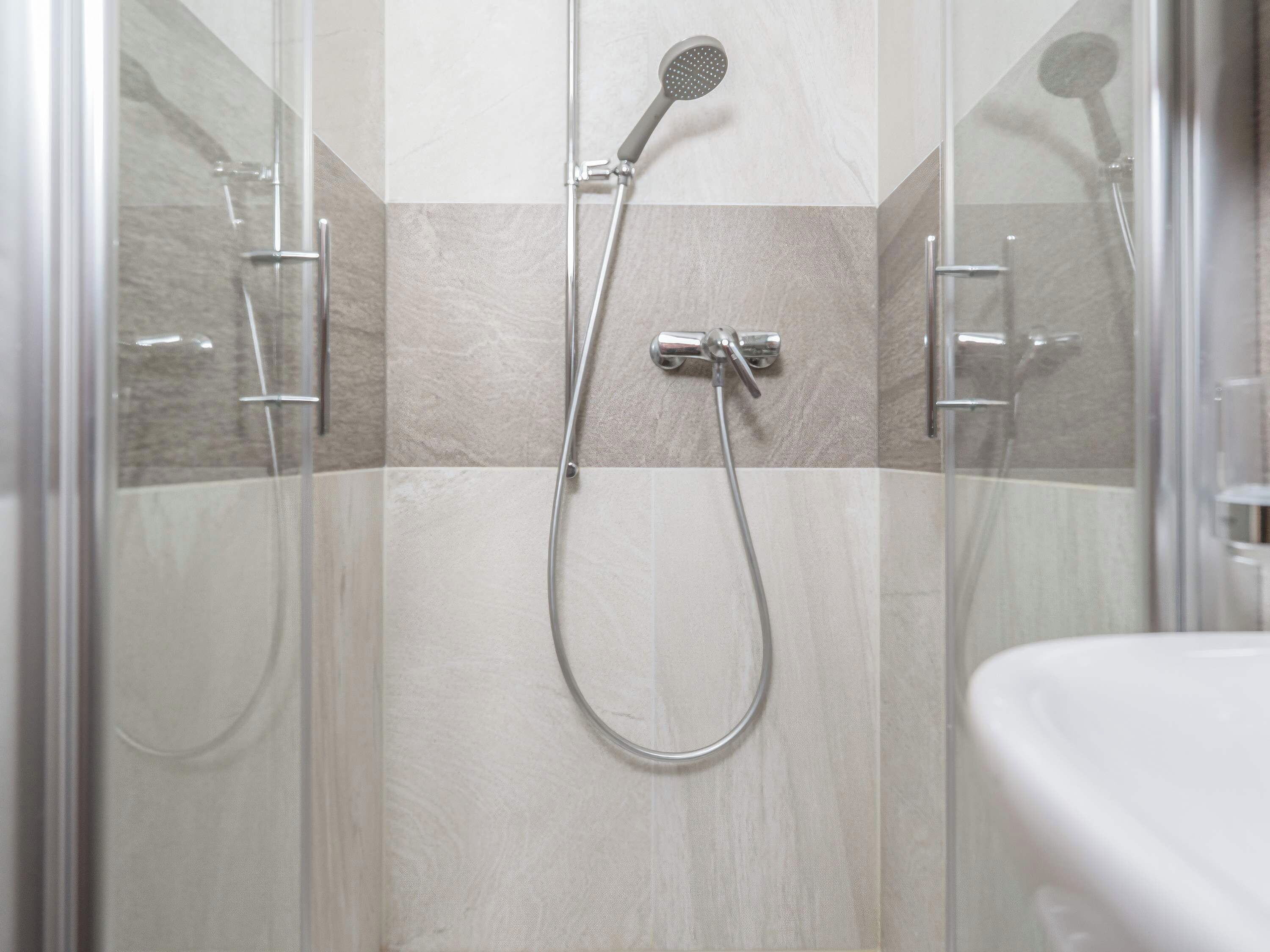 A shower with a handheld showerhead and a wall-mounted faucet.