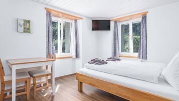Une chambre à coucher avec un lit, un bureau et une chaise. Il y a deux fenêtres avec des rideaux.