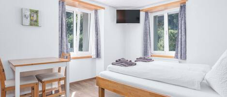A bedroom with a bed, a desk, and a chair. There are two windows with curtains.