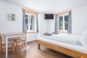 Une chambre à coucher avec un lit, un bureau et une chaise. Il y a deux fenêtres avec des rideaux.