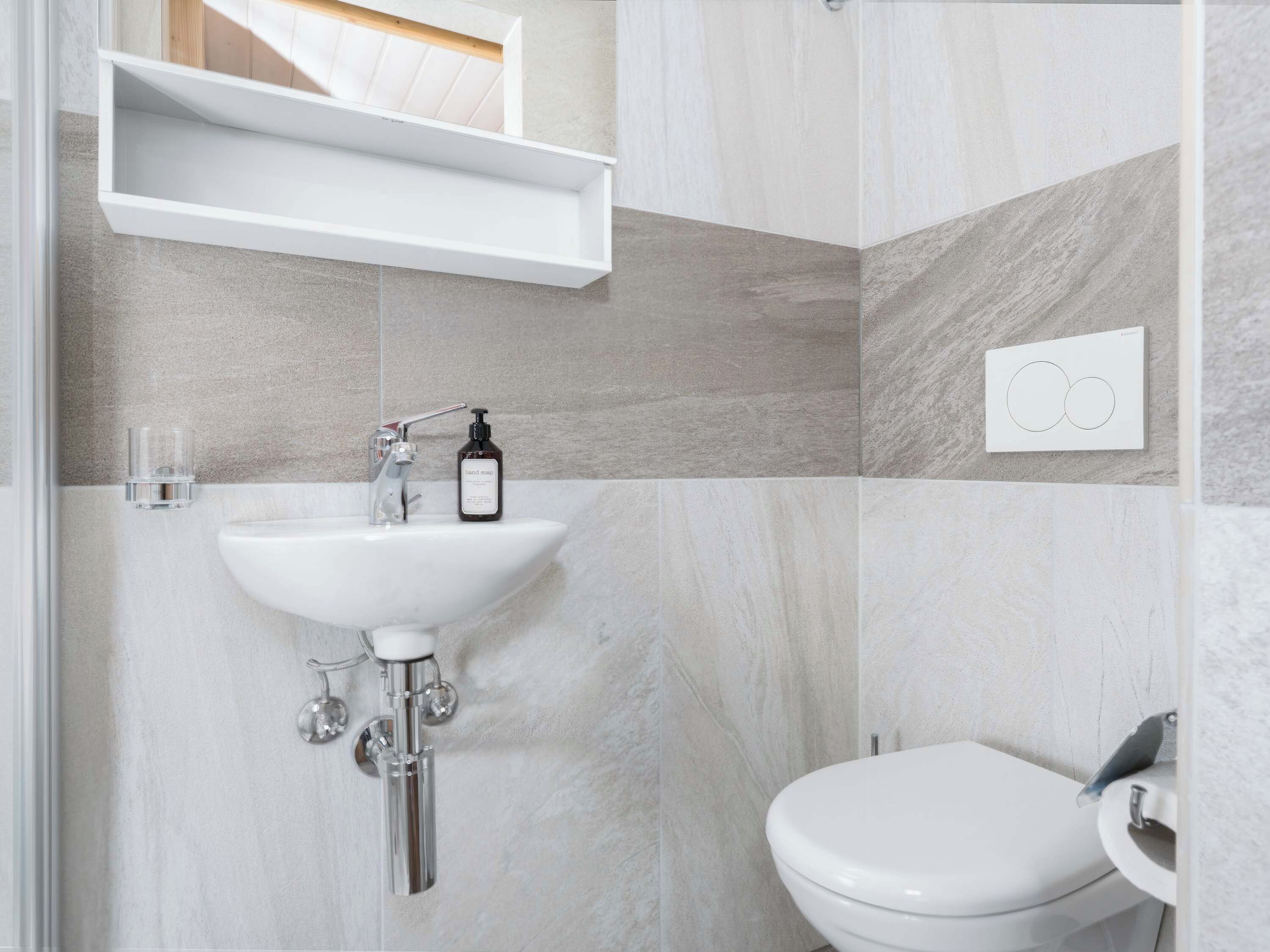 Une salle de bain avec un lavabo blanc, des toilettes et une étagère au-dessus du lavabo.