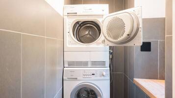 Une machine à laver et un sèche-linge superposés dans une salle de bain aux murs carrelés, avec un banc en bois.