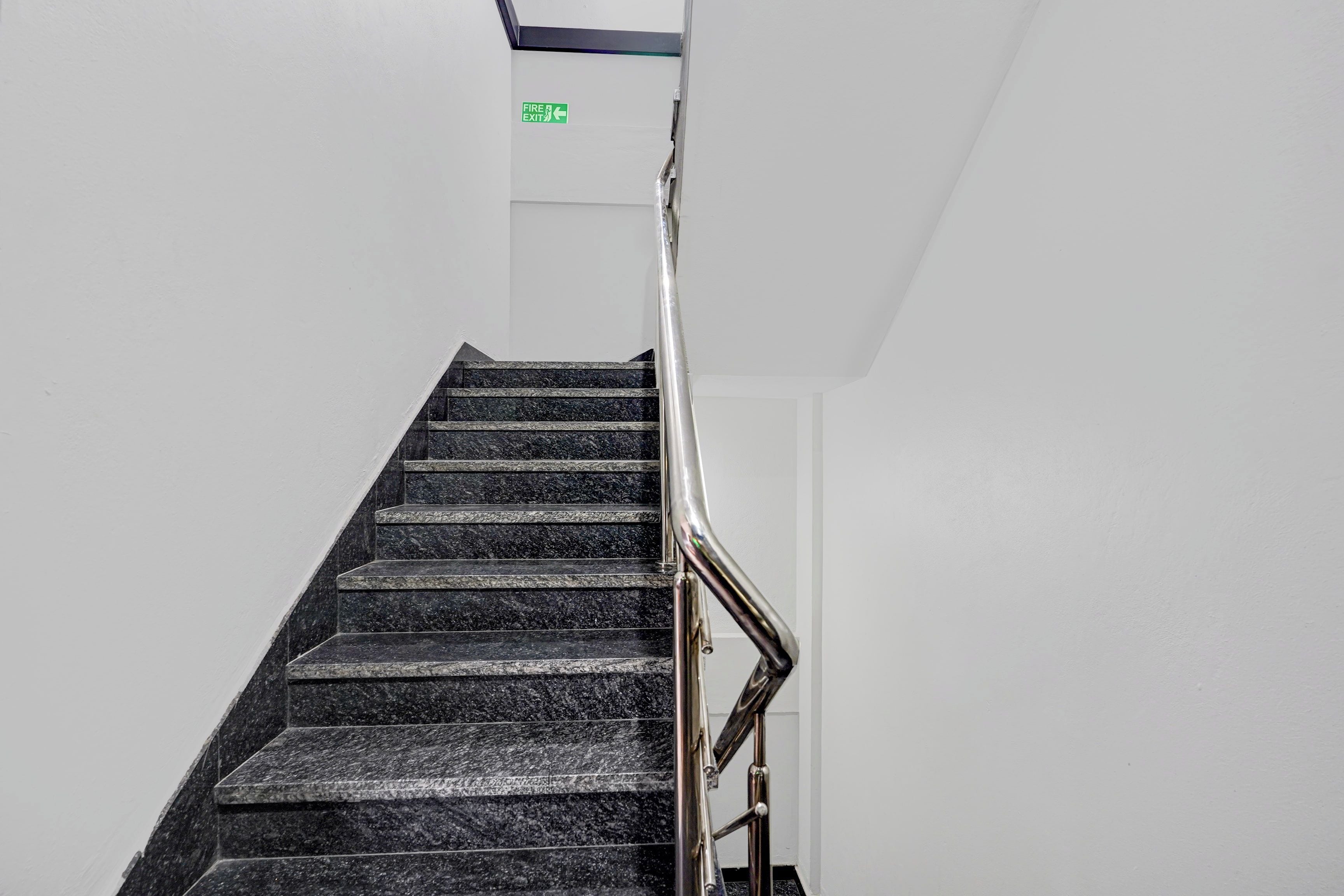 A staircase with a handrail and a fire exit sign above.