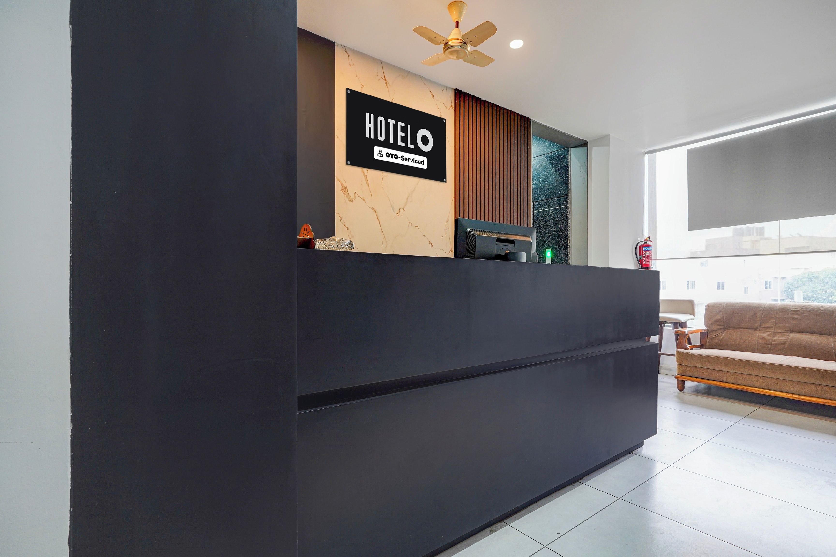 A hotel reception desk with a modern design, a ceiling fan, and a view of the outside through a window.