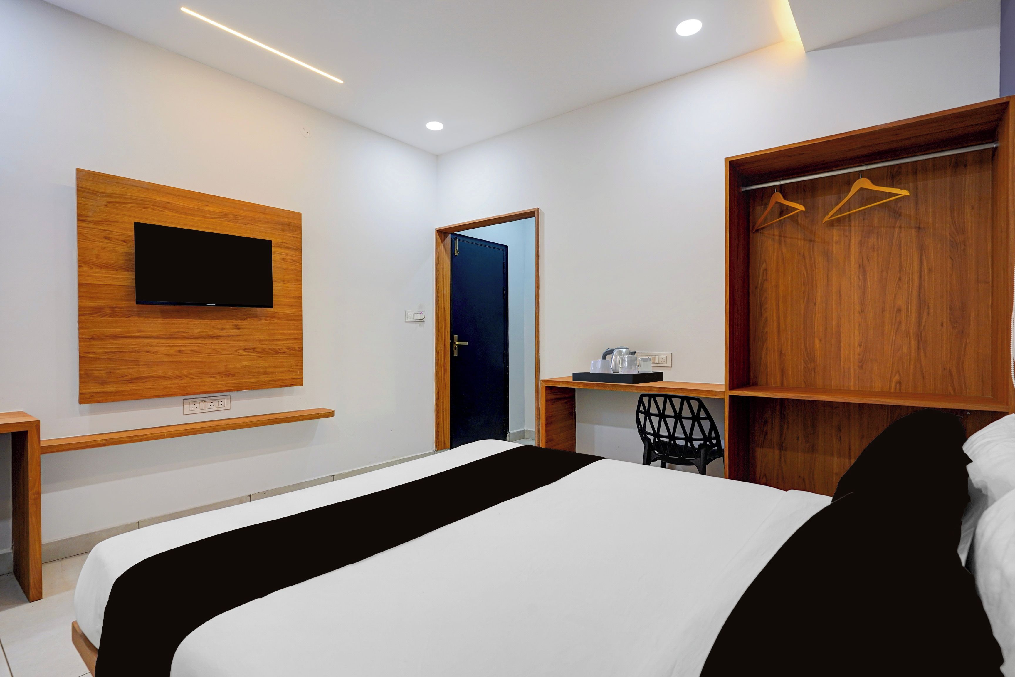 A modern hotel room with a bed, a desk, a wardrobe, and a television mounted on the wall.