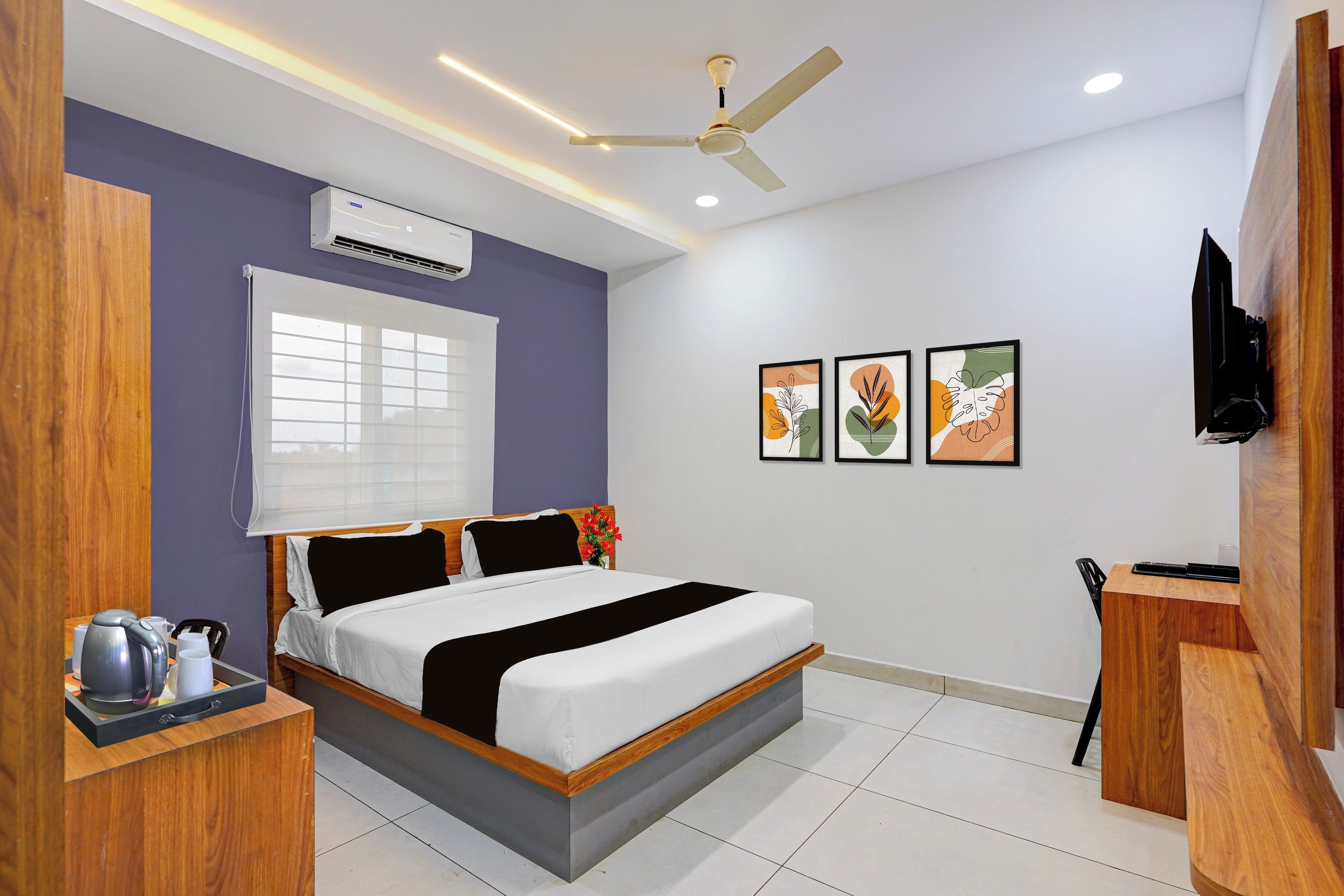 A hotel room with a bed, a desk, a kettle, a coffee maker, a TV, and a ceiling fan.