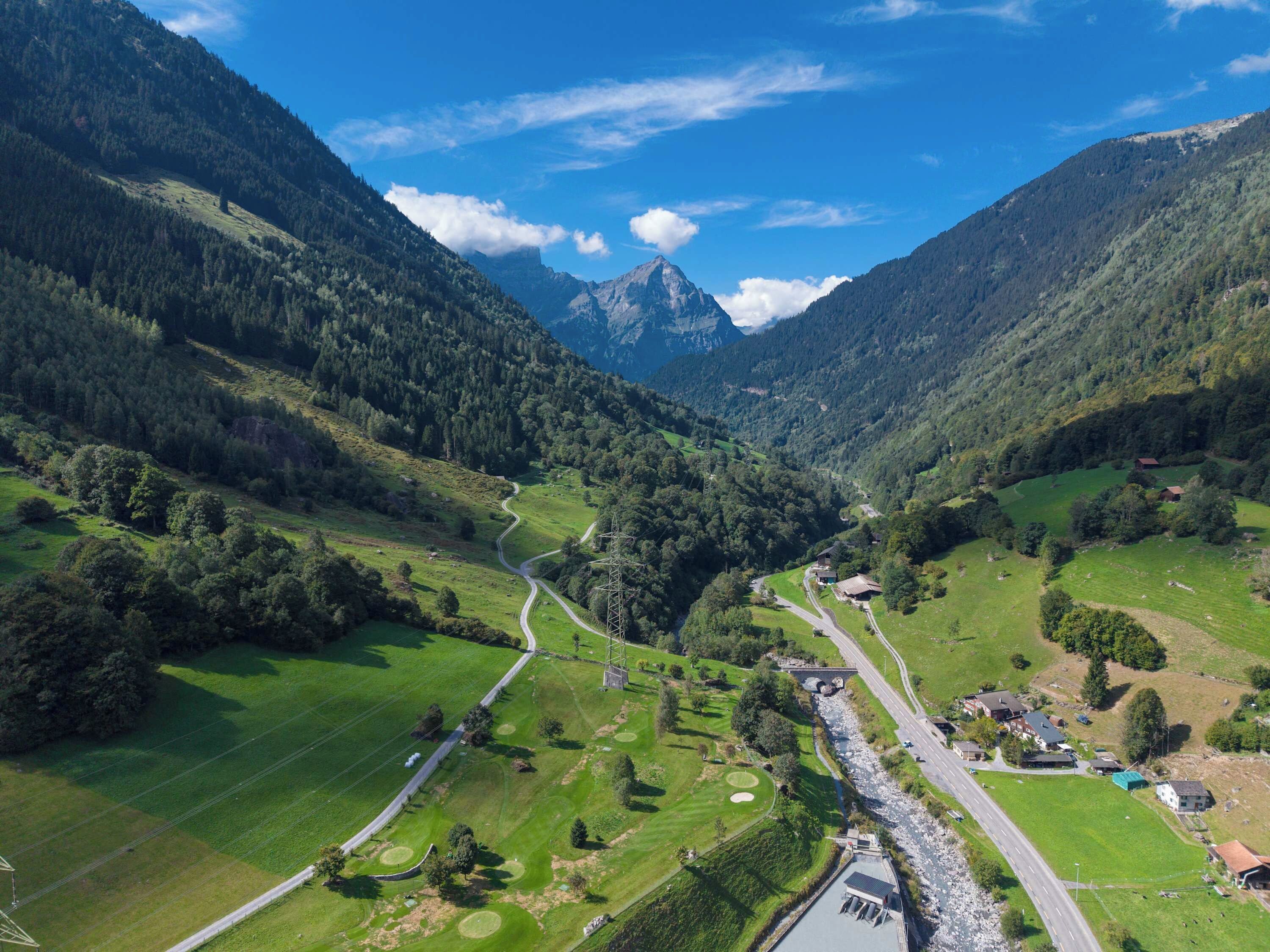 Une vallée traversée par une route sinueuse, un petit village et une montagne en arrière-plan.