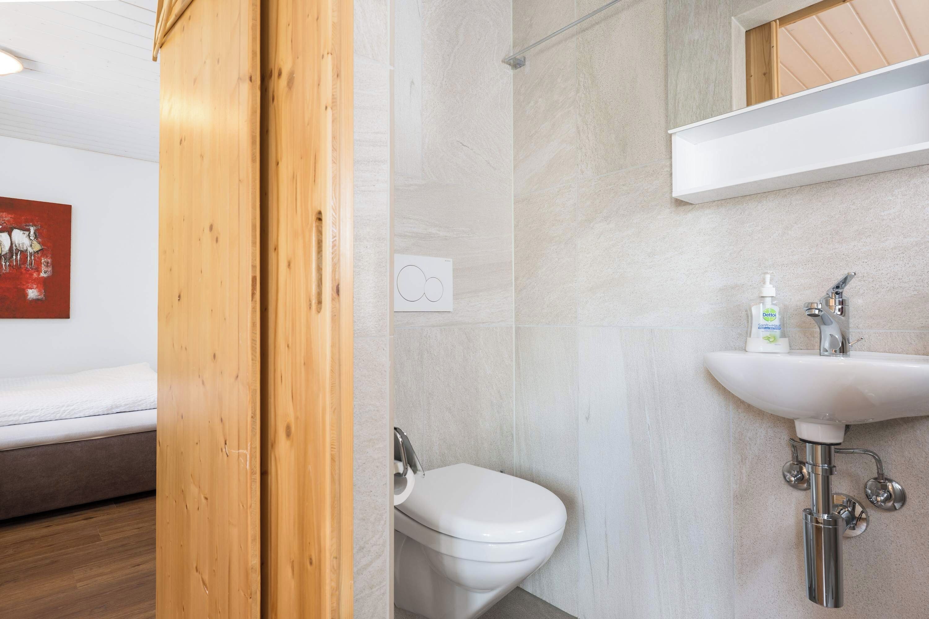 Et moderne badeværelse med et hvidt toilet, en vask med et håndholdt armatur og et bruseområde.