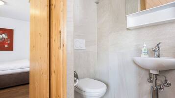 Et moderne badeværelse med et hvidt toilet, en vask med et håndholdt armatur og et bruseområde.
