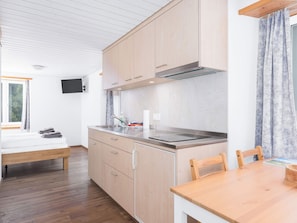 A modern kitchen with wooden cabinets, a built-in stove, and a dining area with a wooden table and chairs. - Private Room near Elm, Kitchenette & Bath (Glarus Süd)