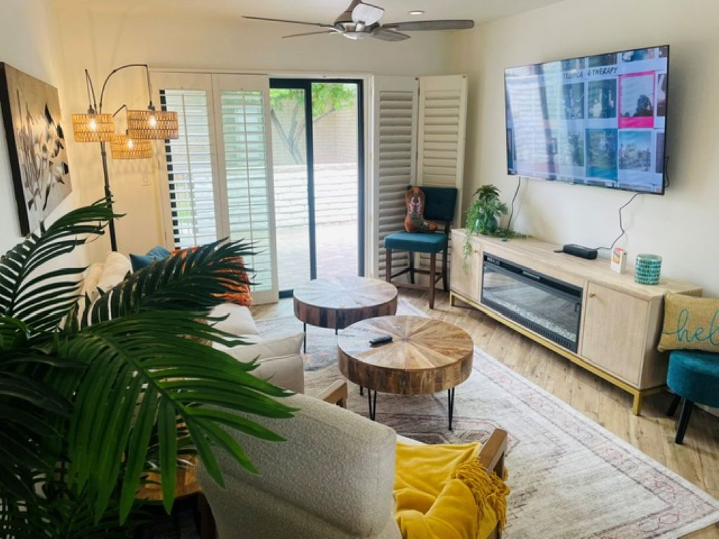 A living room with a sofa, two round coffee tables, a television mounted on the wall, and a sliding glass door leading to an outdoor area.