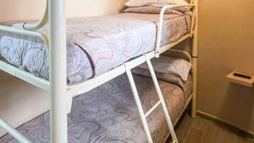 Una cama litera con colchón estampado, estructura metálica y un estante pequeño con un control remoto.