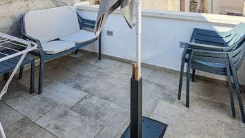 Eine Dachterrasse mit Gartenmöbeln, darunter ein Tisch und Stühle, sowie eine Metallkonstruktion, möglicherweise für einen Grill oder eine Barbecue-Anlage.