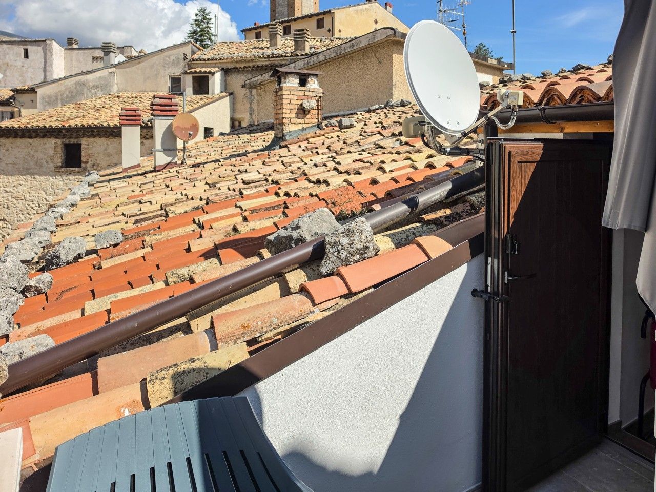 Un balcone con vista su tetti in tegole di terracotta, un'antenna parabolica e una porta che dà su un ambiente interno.
