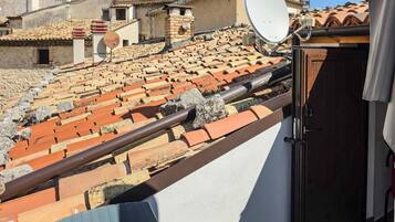 Un balcone con vista su tetti in tegole di terracotta, un'antenna parabolica e una porta che dà su un ambiente interno.