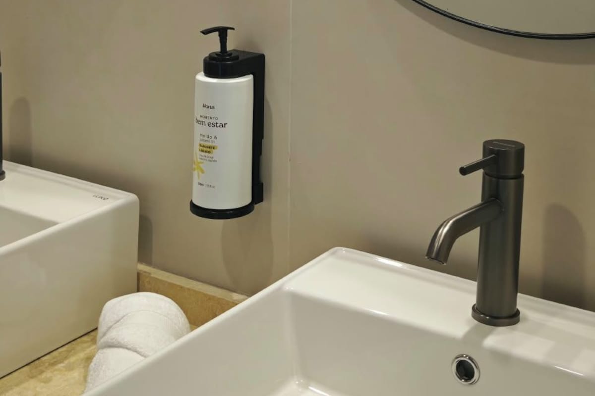 Un baño con dos lavamanos, un espejo y una botella de desinfectante para manos.