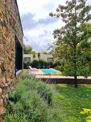 Un edificio de piedra con piscina, rodeado de follaje y un árbol.