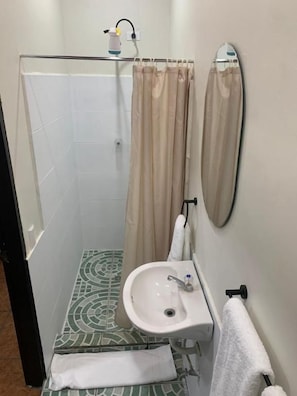 A small bathroom with a shower, a sink, and a mirror.