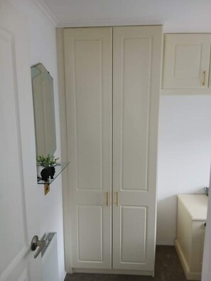 A room with a white wardrobe, a mirror, and a small shelf with a plant.