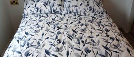 A bed with a floral pattern, two pillows, and two folded blankets.