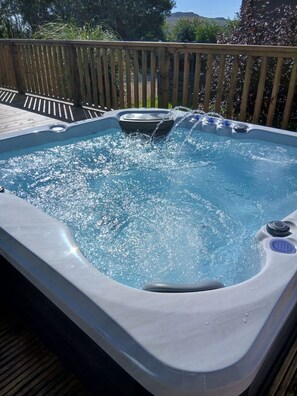 A hot tub with water jets, surrounded by a wooden deck and a wooden fence.