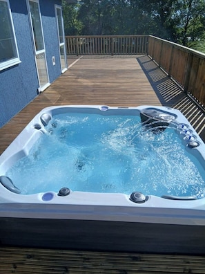 A hot tub on a wooden deck with a blue wall in the background.