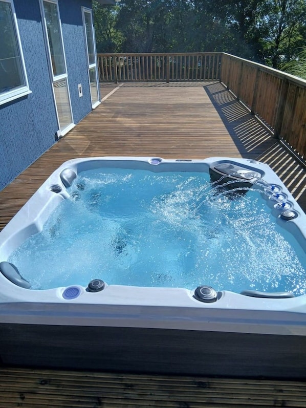 A hot tub on a wooden deck with a blue wall in the background.