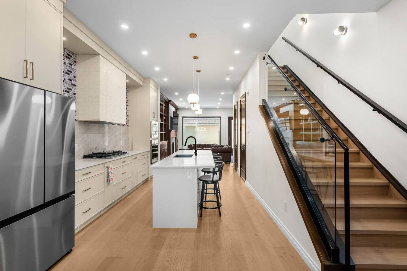 A modern kitchen with a central island, stainless steel appliances, and a staircase with glass railings.