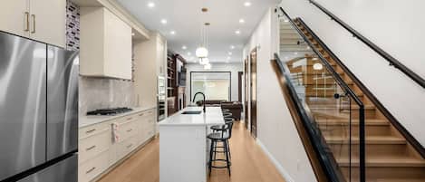 A modern kitchen with a central island, stainless steel appliances, and a staircase with glass railings.