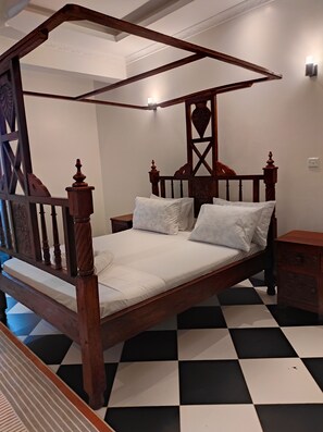A four-poster bed with a wooden frame and white bedding, a nightstand with a drawer, and a checkered floor. - Spacious and Elegant 2-bedroom apartment with AC in Diani Beach (Diani Beach)