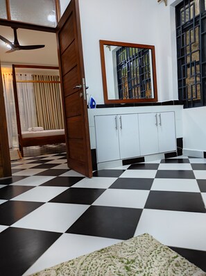 Une pièce avec un sol à carreaux, une armoire blanche aux poignées argentées, un miroir au-dessus de l’armoire et une porte donnant sur une autre pièce.