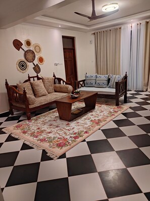 Ein Wohnzimmer mit einer Couch, einem Couchtisch, einem gemusterten Teppich, einem Deckenventilator und einem karierten Boden.