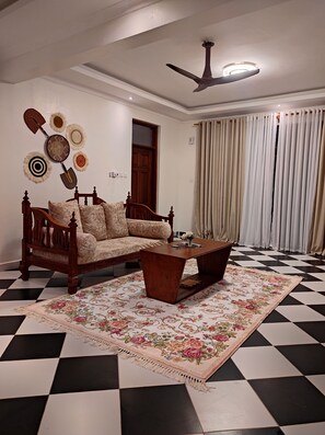 A room with a checkered floor, a wooden sofa, a coffee table, and a ceiling fan. - Spacious and Elegant 2-bedroom apartment with AC in Diani Beach (Diani Beach)