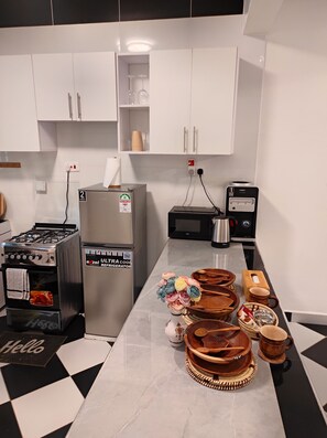 Eine Küche mit weißen Schränken, einem Herd, einem Kühlschrank, einer Mikrowelle und einer Kaffeemaschine.