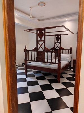 A four-poster bed with a checkered floor, a ceiling fan, and a nightstand. - Spacious and Elegant 2-bedroom apartment with AC in Diani Beach (Diani Beach)