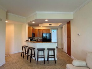 A modern kitchen with a central island, bar stools, and a refrigerator. - Coastal Condo - Near Beach - Bonita Springs (Bonita Springs)