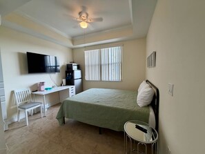 Ein Schlafzimmer mit einem Bett, einem Schreibtisch, einem Sessel, einem Fernseher und einem Deckenventilator.