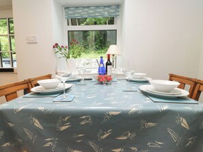A dining table set with white plates, wine glasses, and a blue tablecloth with a leaf pattern. - Puffin Cottage (Bangor)
