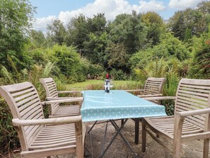 An outdoor seating area with a table and chairs, surrounded by lush greenery. - Puffin Cottage (Bangor)