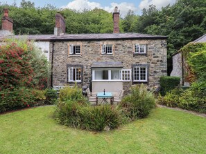 Une maison en pierre avec un jardin, une table et des chaises à l’extérieur.