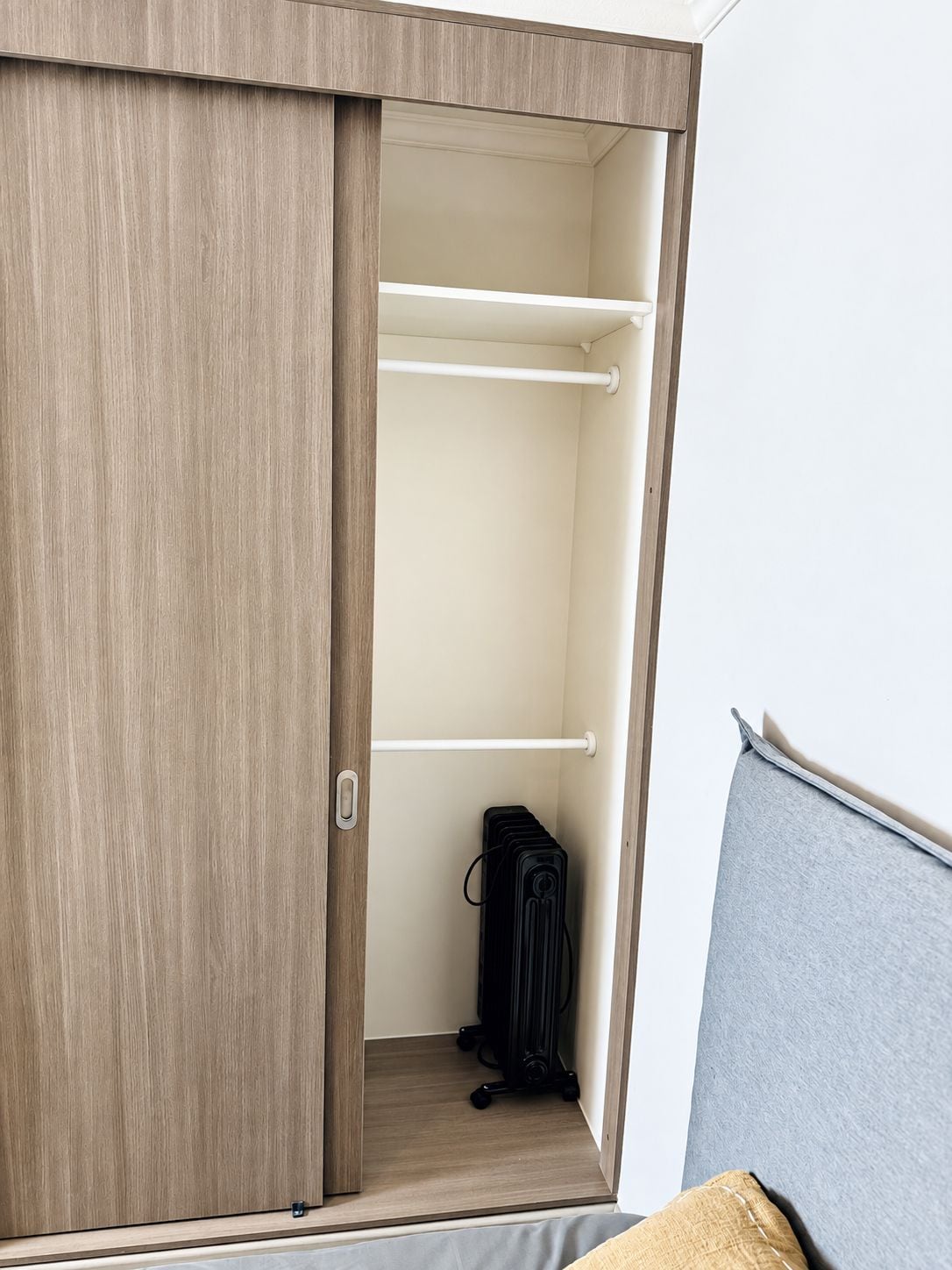 A wardrobe with a sliding door, a hanging rod, and a suitcase on the floor.